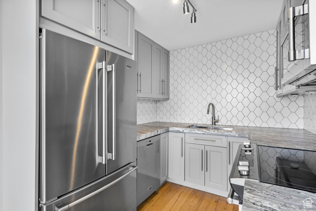 Kitchen with a sink, light stone counters, light wood-type flooring, backsplash, and appliances with stainless steel finishes