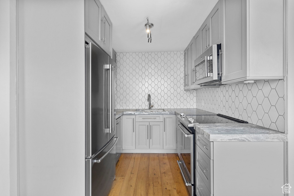 Kitchen featuring a sink, tasteful backsplash, light wood-style flooring, gray cabinetry, and appliances with stainless steel finishes