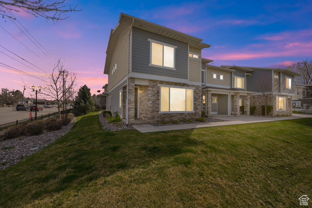 Back of property at dusk with stone siding, fence, and a lawn