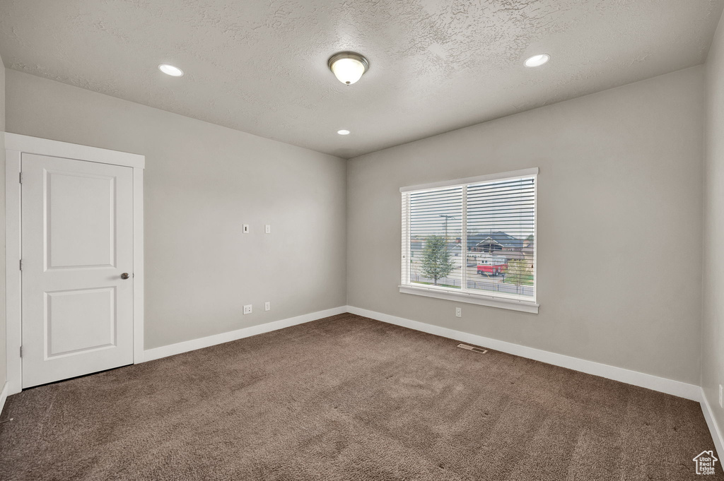 Unfurnished room with a textured ceiling, carpet, baseboards, and visible vents
