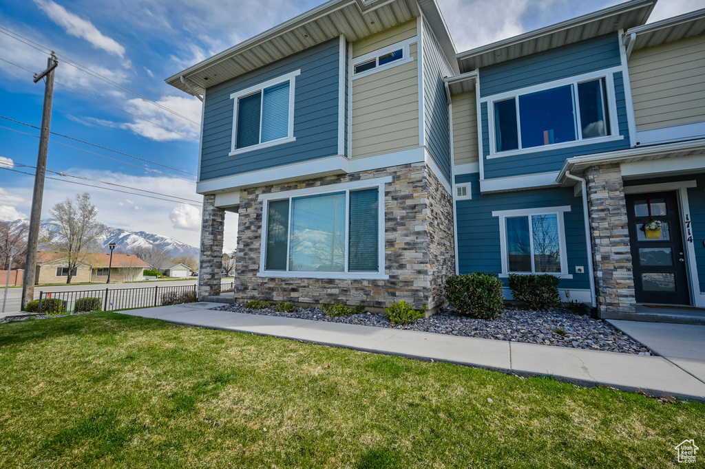 Exterior space with stone siding, a front lawn, fence, and a mountain view