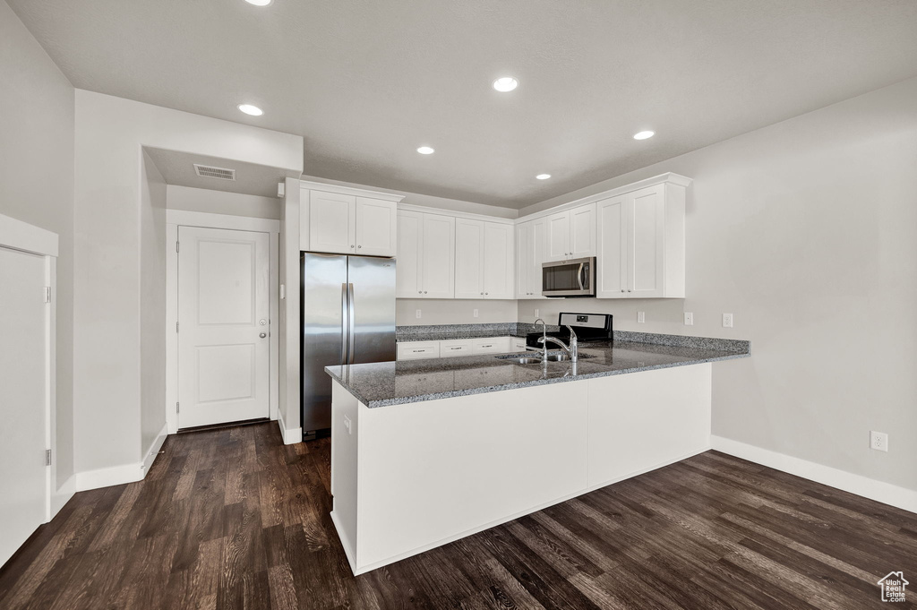Kitchen featuring a sink, a peninsula, stainless steel appliances, dark stone countertops, and baseboards