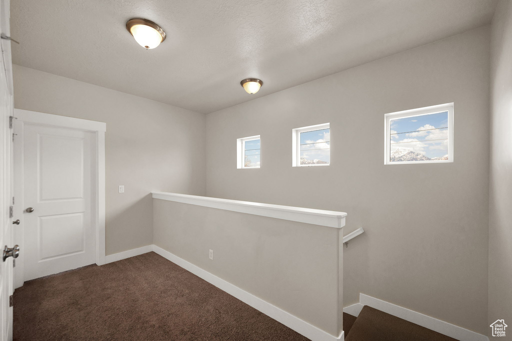 Hallway featuring baseboards, dark carpet, and an upstairs landing