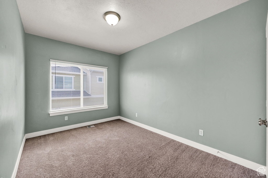Carpeted empty room featuring a textured ceiling, baseboards, and visible vents