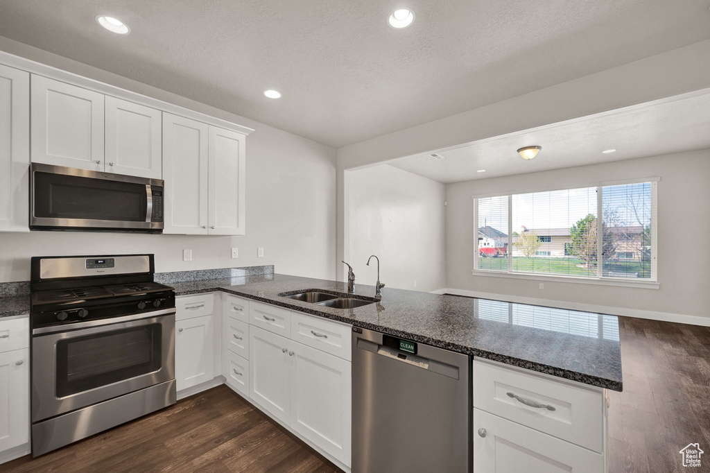 Kitchen featuring a sink, a peninsula, dark stone counters, dark wood-type flooring, and appliances with stainless steel finishes