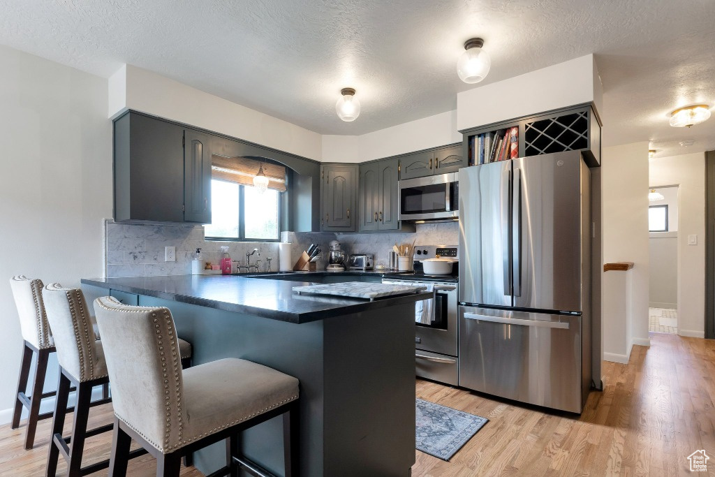 Kitchen featuring a kitchen bar, a peninsula, decorative backsplash, dark countertops, and stainless steel appliances