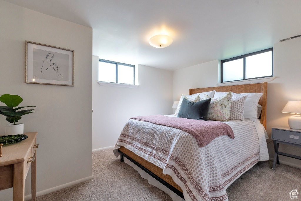Bedroom featuring light colored carpet, baseboards, visible vents, and multiple windows