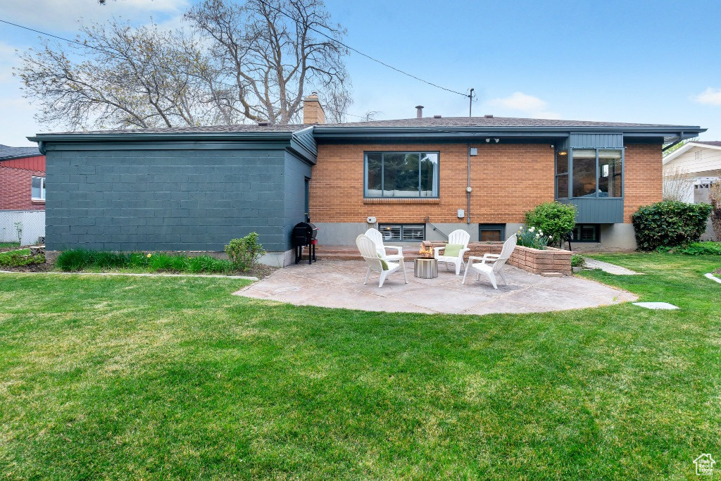 Back of property featuring brick siding, a patio area, a chimney, and a lawn