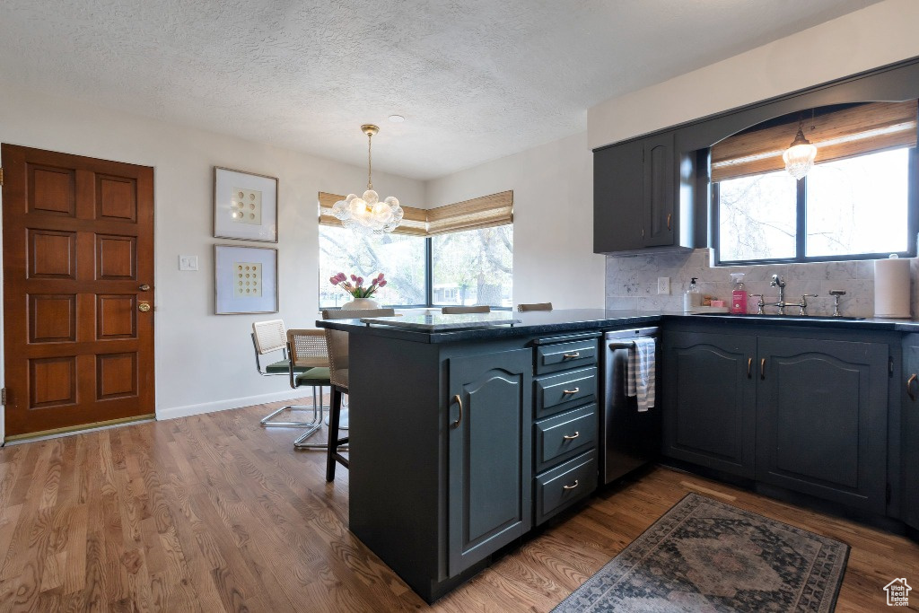 Kitchen featuring a sink, a peninsula, dishwashing machine, a notable chandelier, and dark countertops