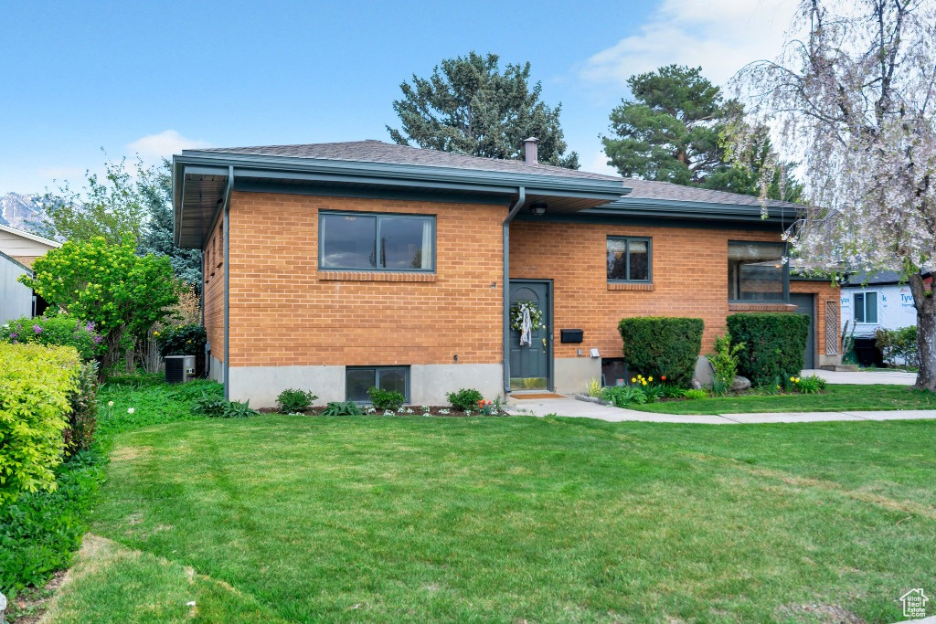 Raised ranch featuring central air condition unit, a front lawn, and brick siding