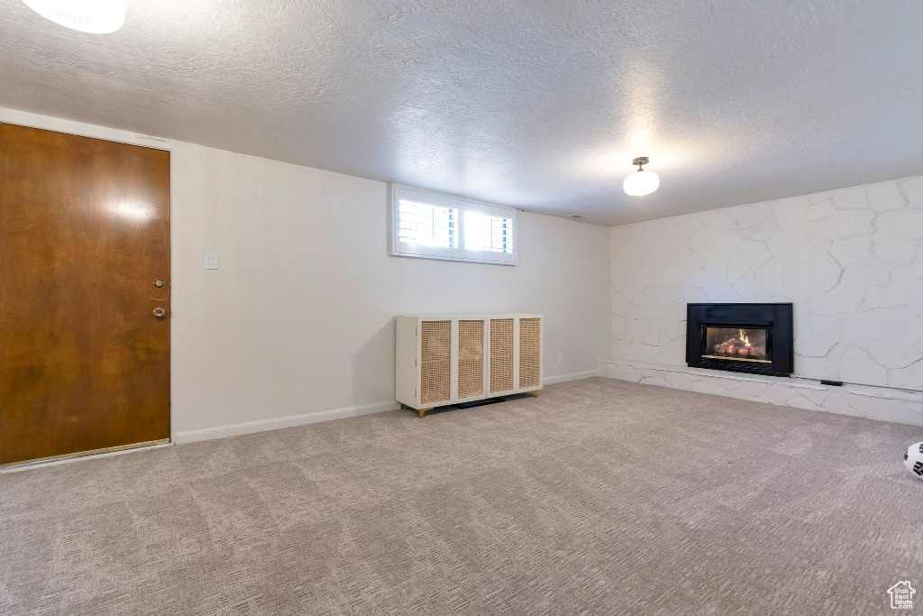 Basement with a textured ceiling, visible vents, a stone fireplace, and carpet floors