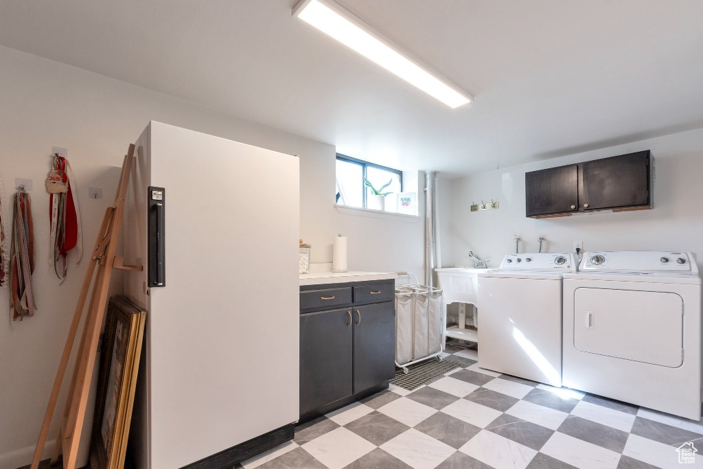 Clothes washing area with a sink, separate washer and dryer, light floors, and cabinet space
