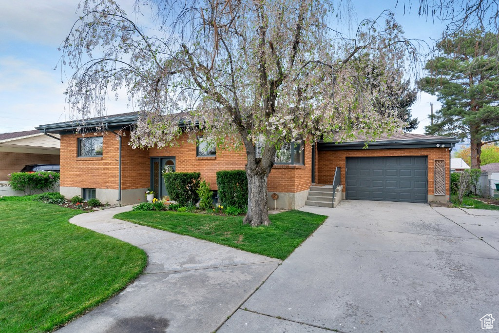 Bi-level home featuring a front lawn, driveway, brick siding, and a garage