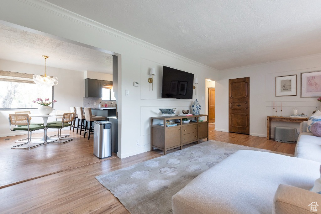 Living area with light wood-type flooring, a chandelier, baseboards, and ornamental molding
