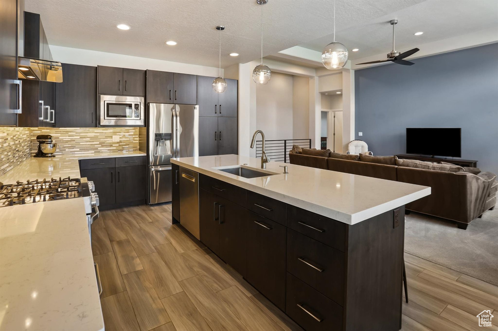 Kitchen with appliances with stainless steel finishes, a sink, open floor plan, backsplash, and light wood-type flooring