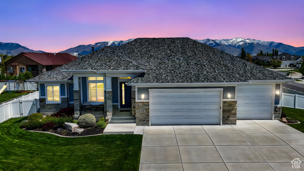 View of front facade featuring fence, a mountain view, stone siding, concrete driveway, and a garage