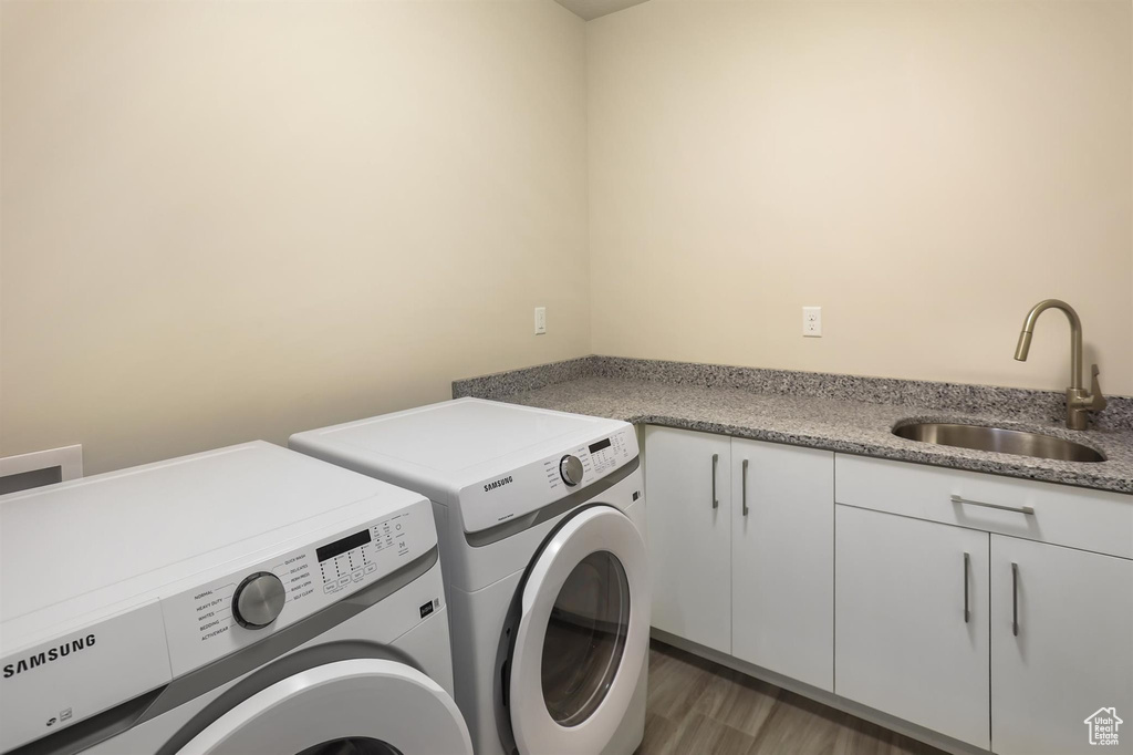 Laundry area with cabinet space, washing machine and clothes dryer, wood finished floors, and a sink