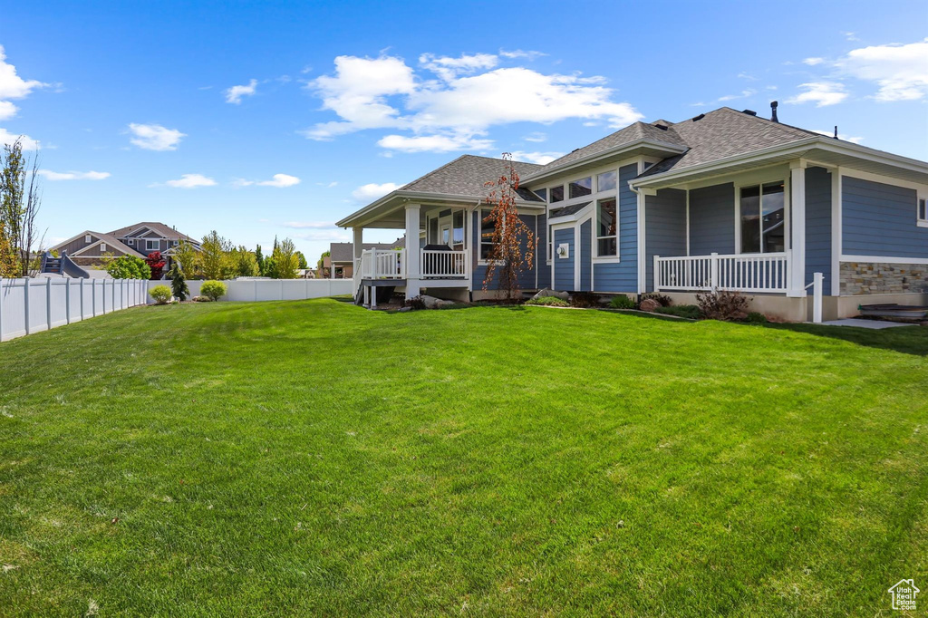 Rear view of property featuring a yard, a shingled roof, covered porch, and a fenced backyard