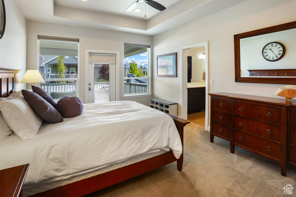 Bedroom with a tray ceiling, multiple windows, ensuite bathroom, and access to exterior