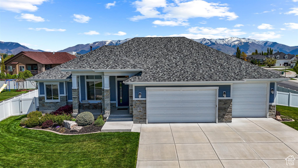 View of front of home featuring an attached garage, a mountain view, stone siding, fence, and concrete driveway