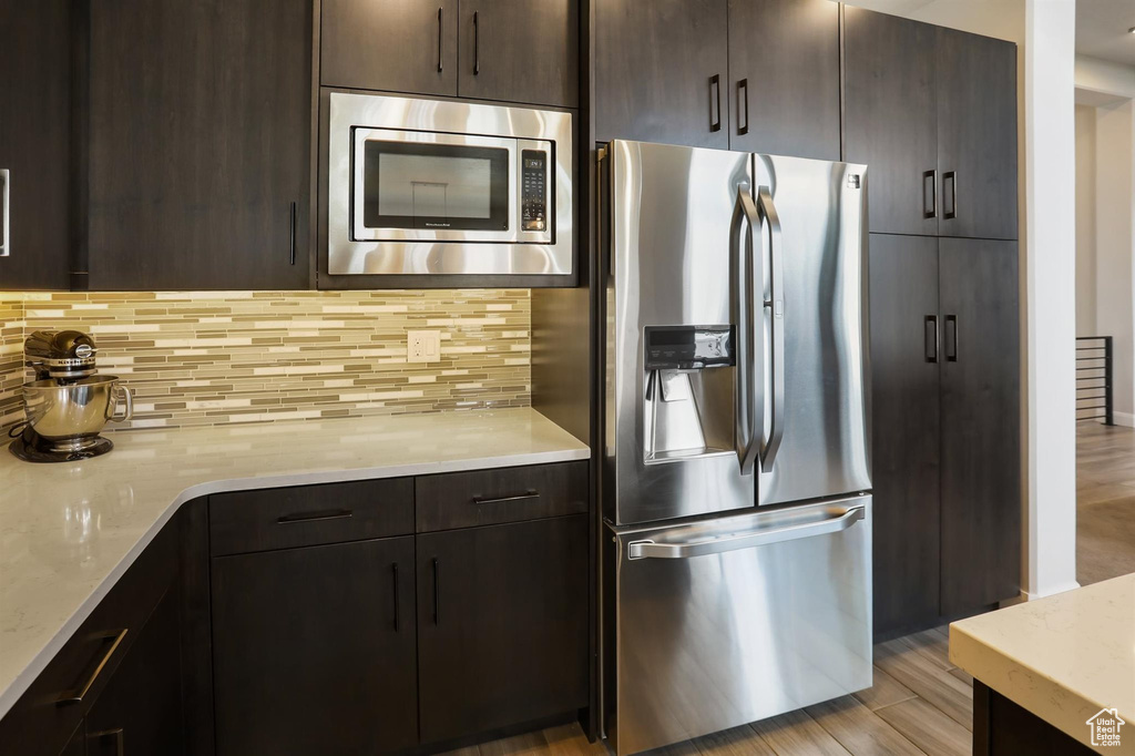 Kitchen with light stone counters, stainless steel appliances, tasteful backsplash, and dark brown cabinets