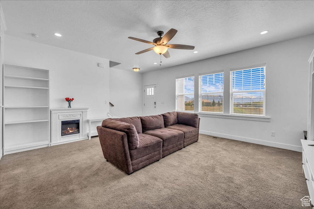 Living area with carpet flooring, a warm lit fireplace, a ceiling fan, and recessed lighting