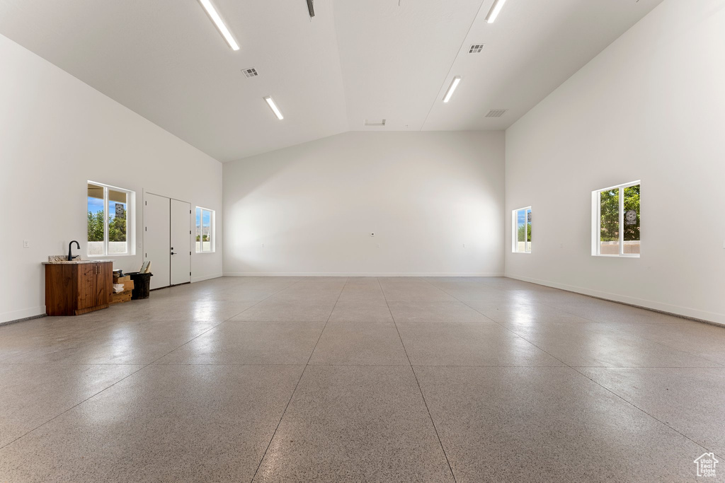 Empty room featuring baseboards, high vaulted ceiling, and light speckled floor