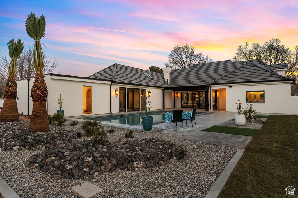 Rear view of property featuring stucco siding, a tile roof, an outdoor pool, and a patio