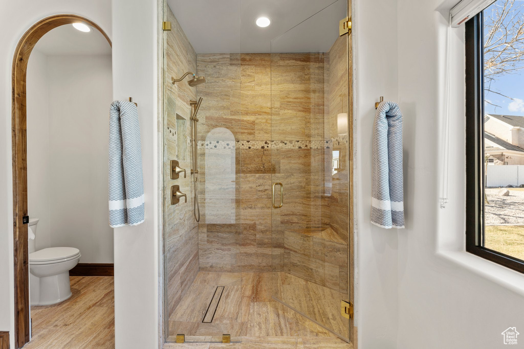 Bathroom with toilet, a stall shower, baseboards, and wood finished floors