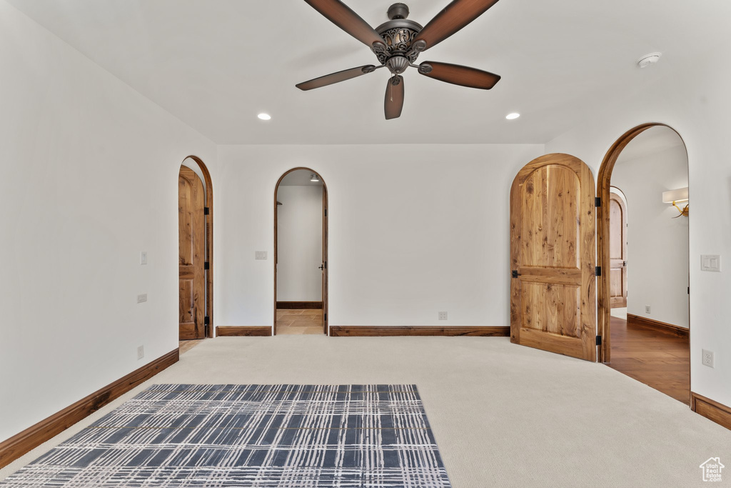 Carpeted empty room featuring arched walkways, ceiling fan, baseboards, and recessed lighting