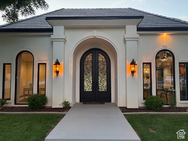 View of exterior entry featuring stucco siding, a tiled roof, and a lawn