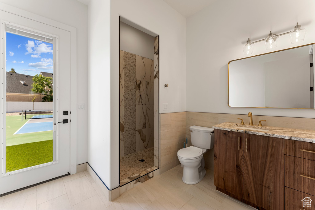Full bath with toilet, tile walls, a wainscoted wall, vanity, and tiled shower