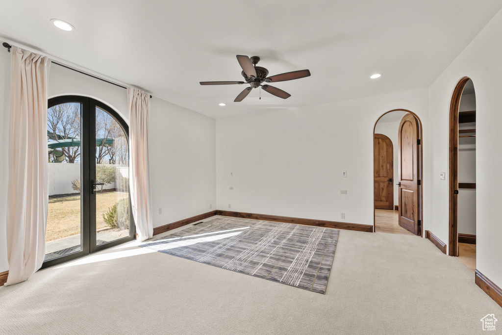 Carpeted spare room featuring a ceiling fan, arched walkways, baseboards, and recessed lighting