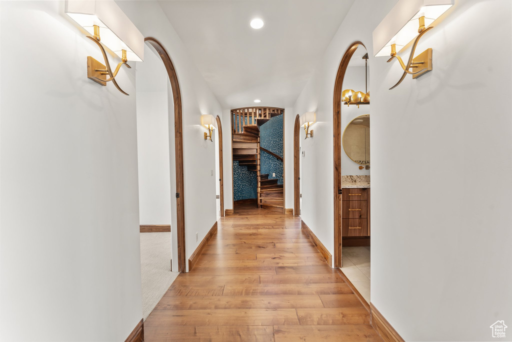 Corridor with light wood finished floors, baseboards, arched walkways, stairs, and recessed lighting