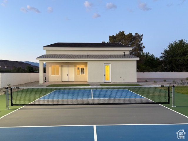 Back of property with stucco siding, fence, a tennis court, metal roof, and a standing seam roof