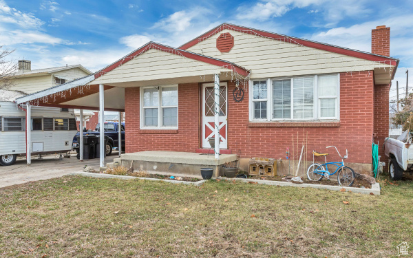 Bungalow-style home featuring an attached carport, a chimney, a front lawn, concrete driveway, and brick siding