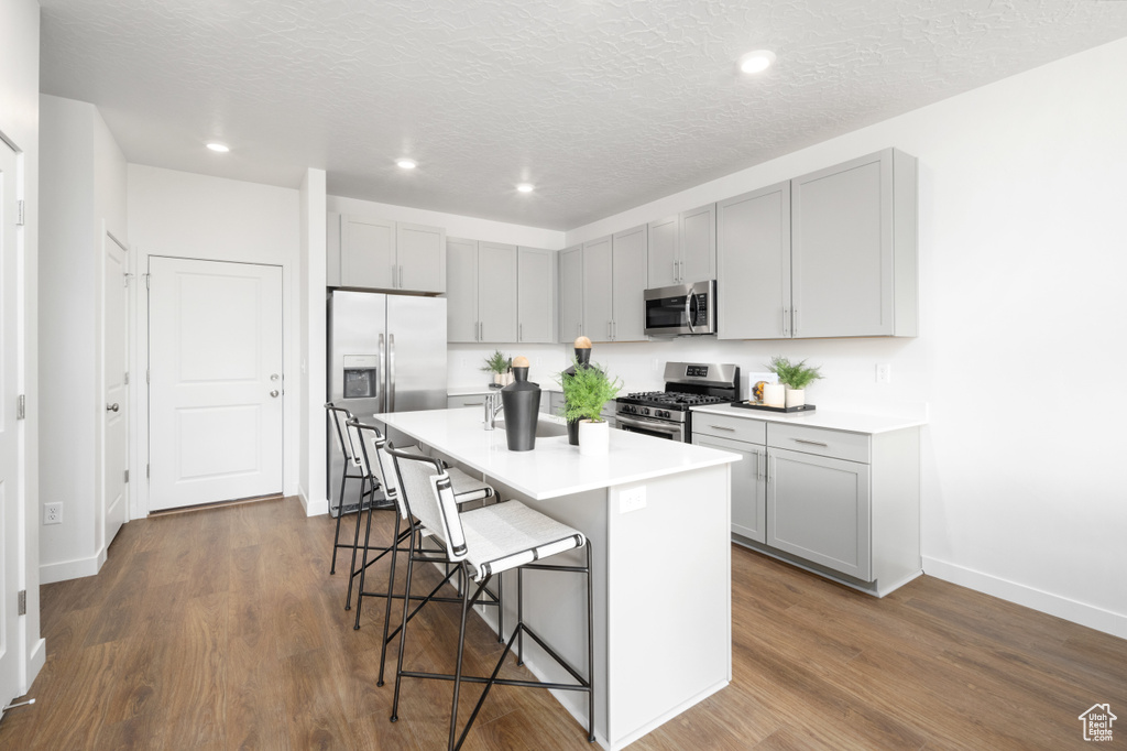 Kitchen featuring a breakfast bar area, gray cabinets, dark wood-style flooring, baseboards, and appliances with stainless steel finishes