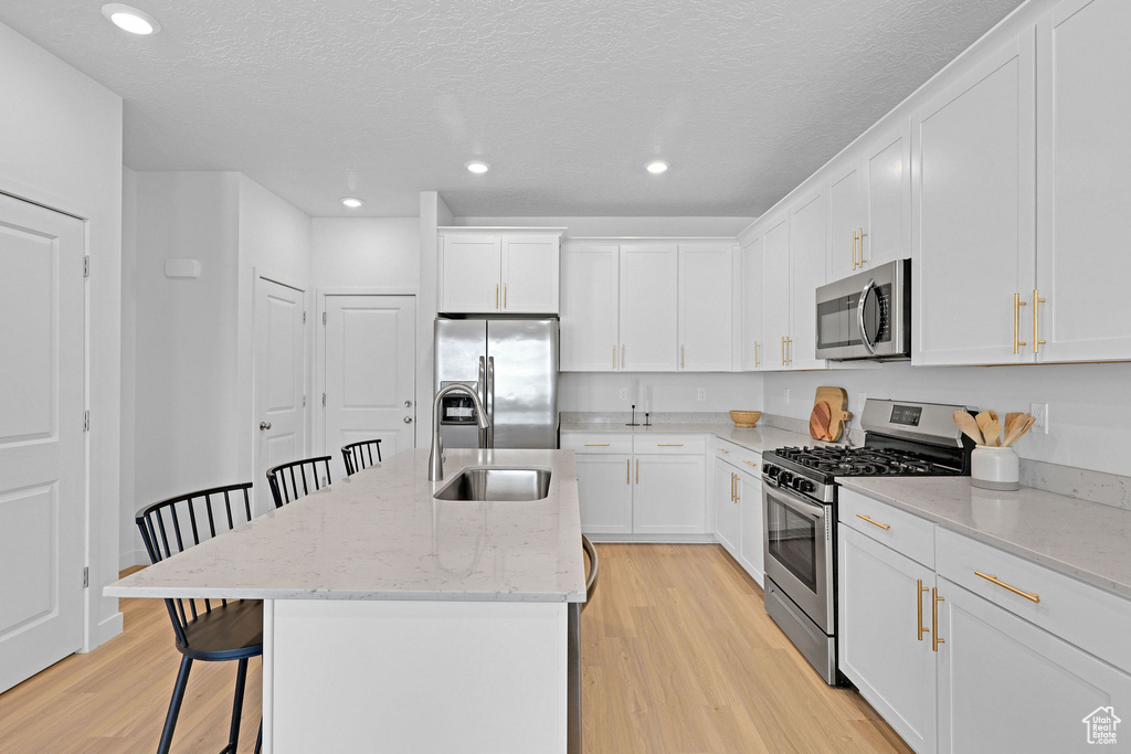 Kitchen featuring a sink, stainless steel appliances, a kitchen island with sink, light wood-type flooring, and a kitchen bar