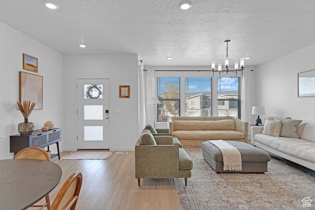 Living area featuring a textured ceiling, wood finished floors, a healthy amount of sunlight, and a notable chandelier