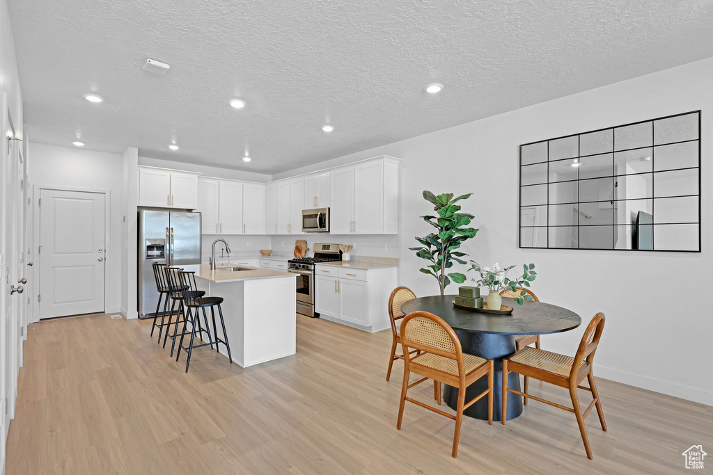 Kitchen featuring light wood finished floors, a kitchen bar, a sink, stainless steel appliances, and light countertops