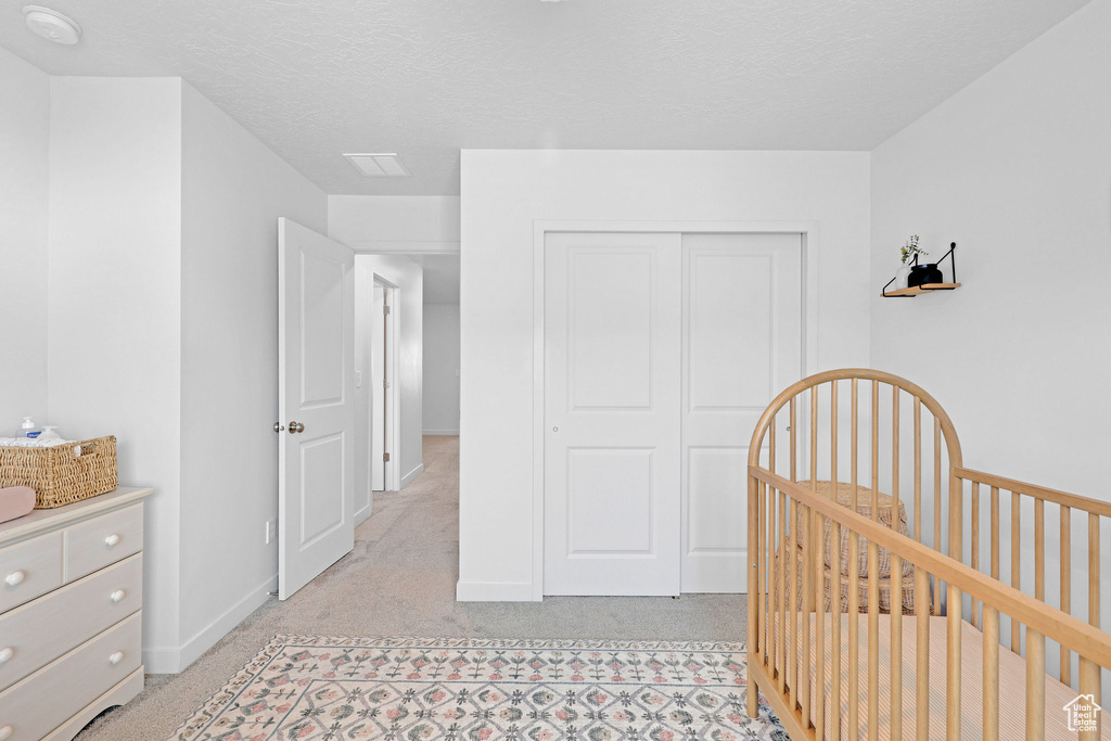 Bedroom with a nursery area, a closet, a textured ceiling, and light carpet