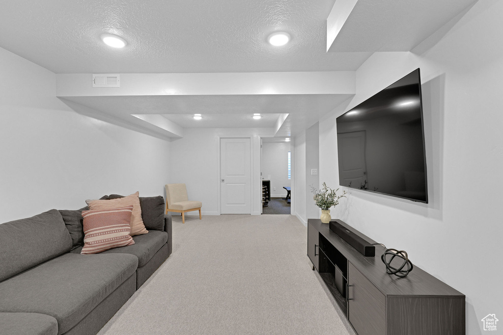 Living area with a textured ceiling, baseboards, visible vents, and light colored carpet