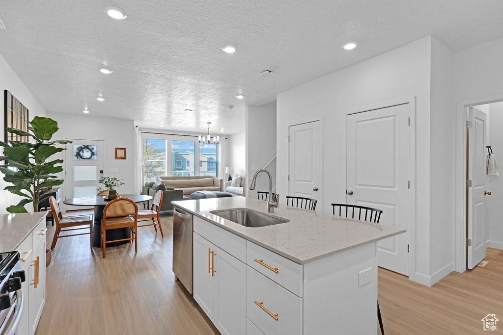 Kitchen with a sink, stainless steel appliances, a notable chandelier, a center island with sink, and light wood-type flooring