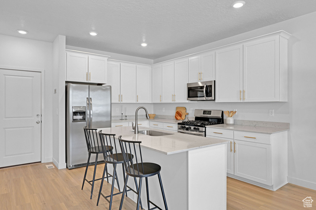Kitchen with a breakfast bar area, a sink, stainless steel appliances, white cabinets, and light wood-style floors