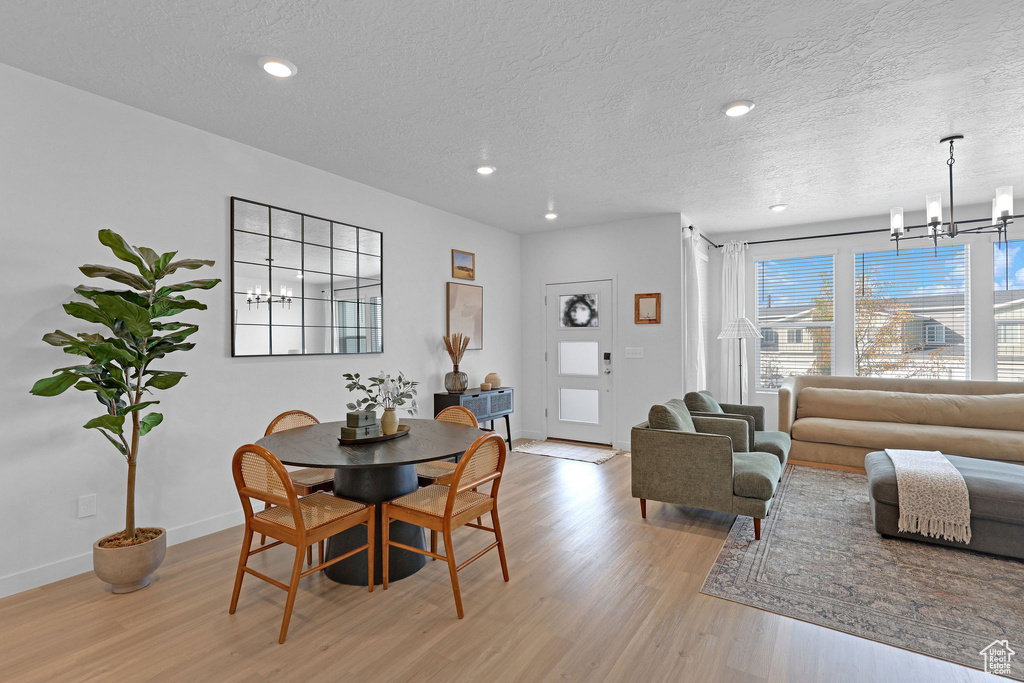 Dining area featuring a chandelier, a textured ceiling, baseboards, and light wood finished floors
