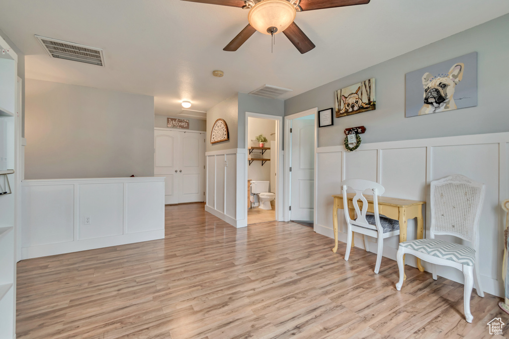 Sitting room with a ceiling fan, visible vents, a decorative wall, a wainscoted wall, and light wood-type flooring