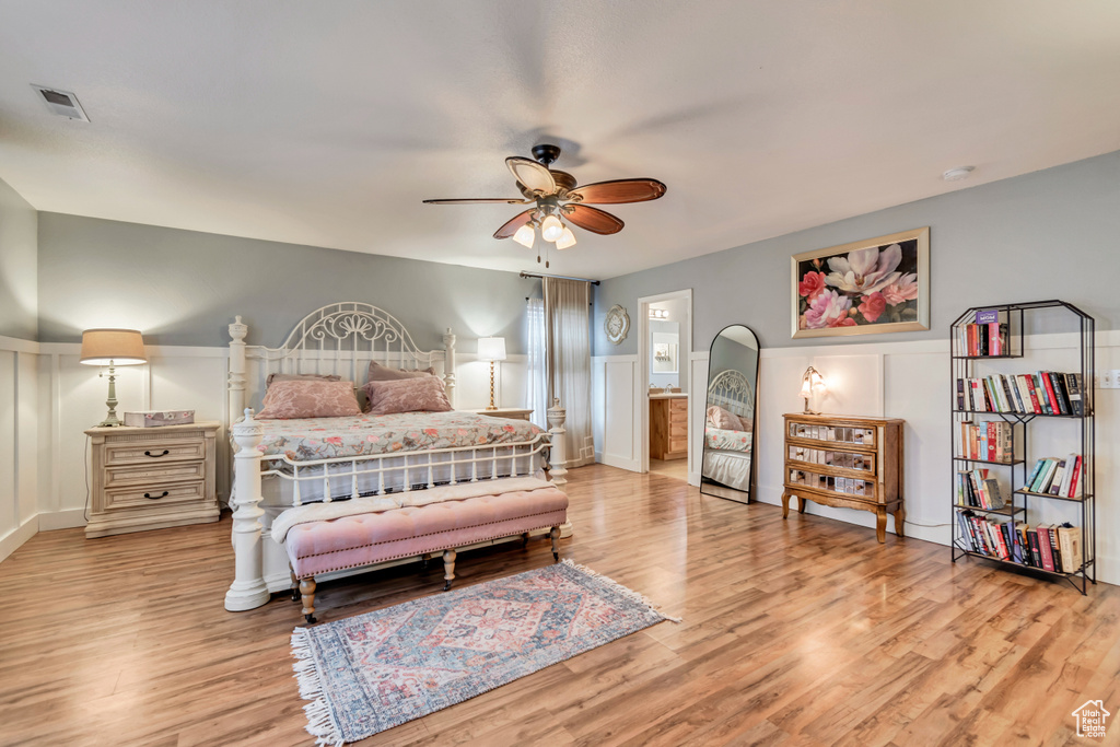 Bedroom with a ceiling fan, light wood finished floors, visible vents, a decorative wall, and a wainscoted wall