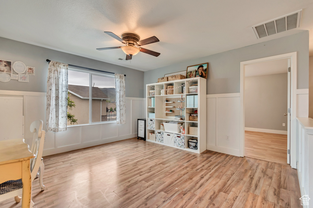 Interior space featuring wood finished floors, a ceiling fan, a wainscoted wall, visible vents, and a decorative wall
