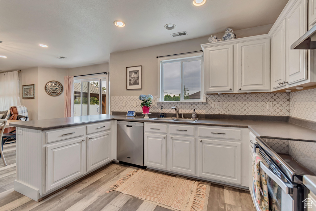 Kitchen featuring a sink, a peninsula, visible vents, dishwasher, and white cabinets