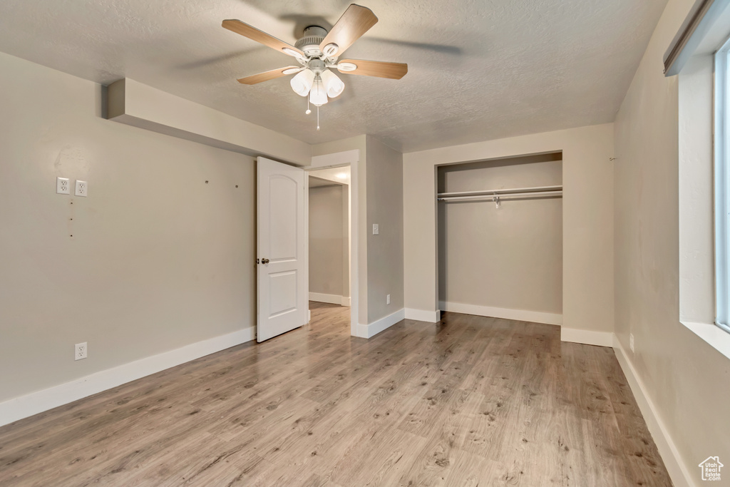 Unfurnished bedroom featuring a ceiling fan, a closet, light wood-style flooring, a textured ceiling, and baseboards
